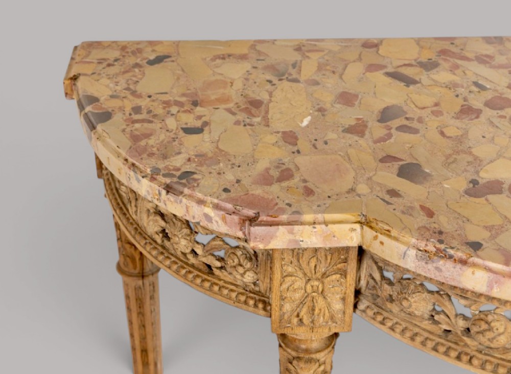 An 18th-century Louis XVI demilune console table featuring a variegated marble top, pierced carved floral frieze, fluted tapered legs, and a decorative central stretcher. View V