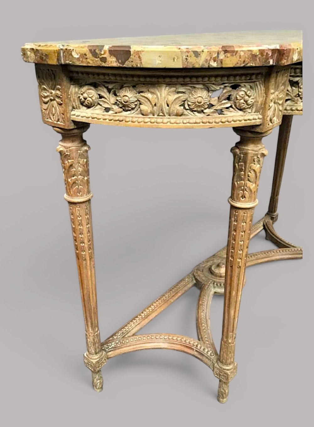 An 18th-century Louis XVI demilune console table featuring a variegated marble top, pierced carved floral frieze, fluted tapered legs, and a decorative central stretcher. View IX