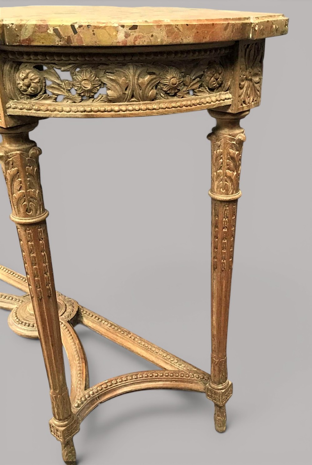 An 18th-century Louis XVI demilune console table featuring a variegated marble top, pierced carved floral frieze, fluted tapered legs, and a decorative central stretcher. View X