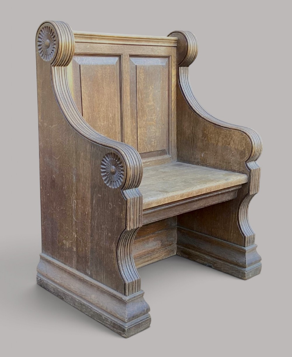 A 19th-century solid oak hall seat featuring a panelled back, carved rosette terminals, and fluted architectural supports.
