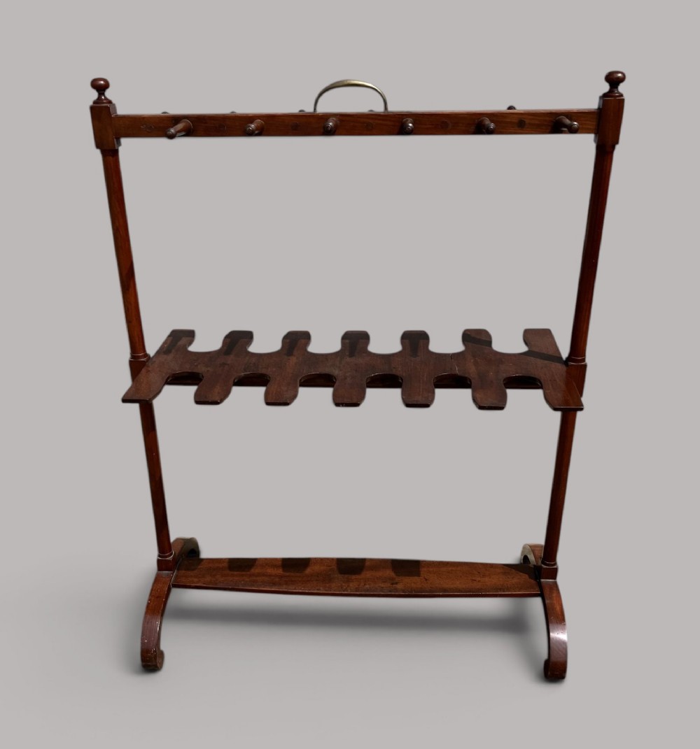An antique mahogany whip and boot stand featuring turned upper pegs, a brass handle, shaped middle boot apertures, and swept trestle feet. View II