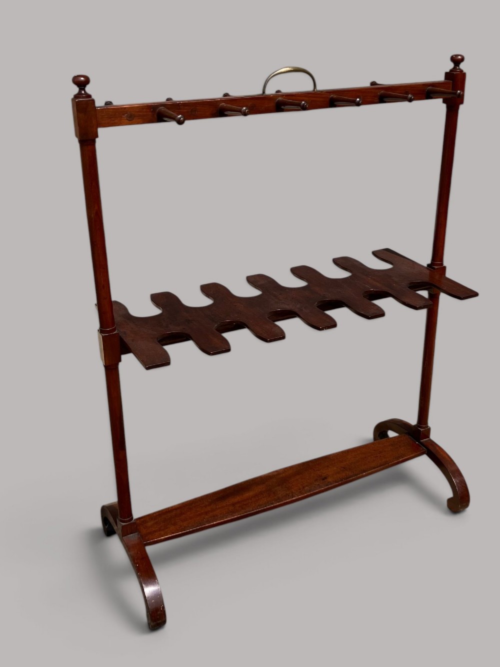 An antique mahogany whip and boot stand featuring turned upper pegs, a brass handle, shaped middle boot apertures, and swept trestle feet. View III
