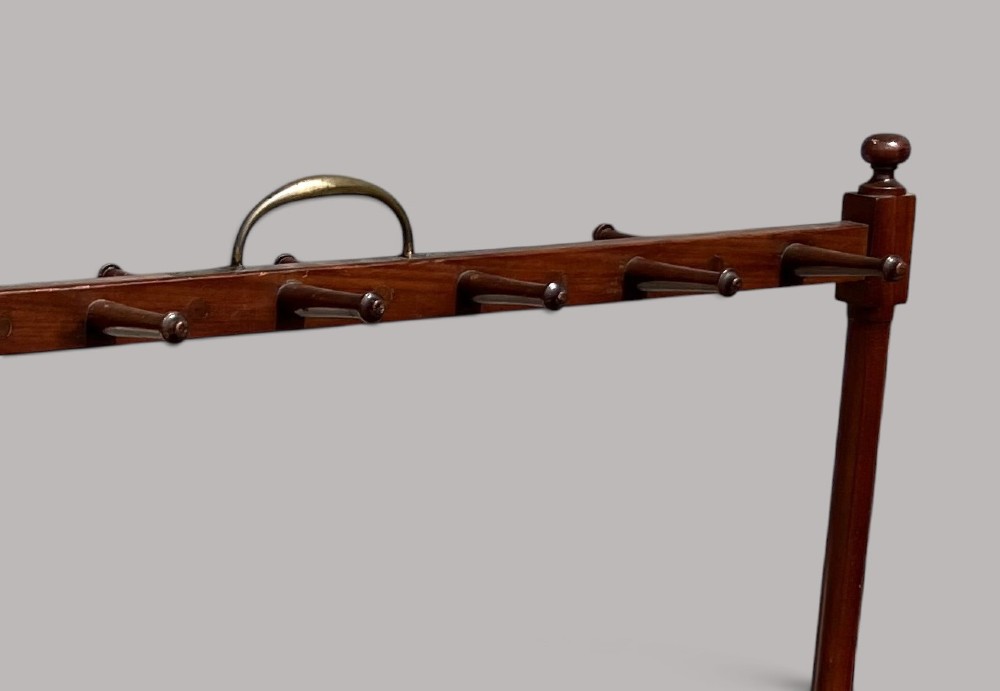 An antique mahogany whip and boot stand featuring turned upper pegs, a brass handle, shaped middle boot apertures, and swept trestle feet. View V