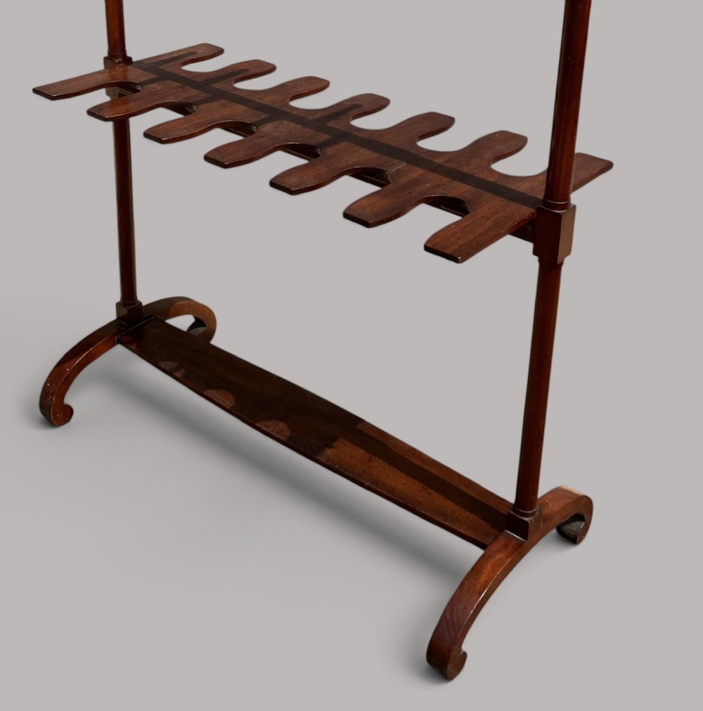 An antique mahogany whip and boot stand featuring turned upper pegs, a brass handle, shaped middle boot apertures, and swept trestle feet. View VI