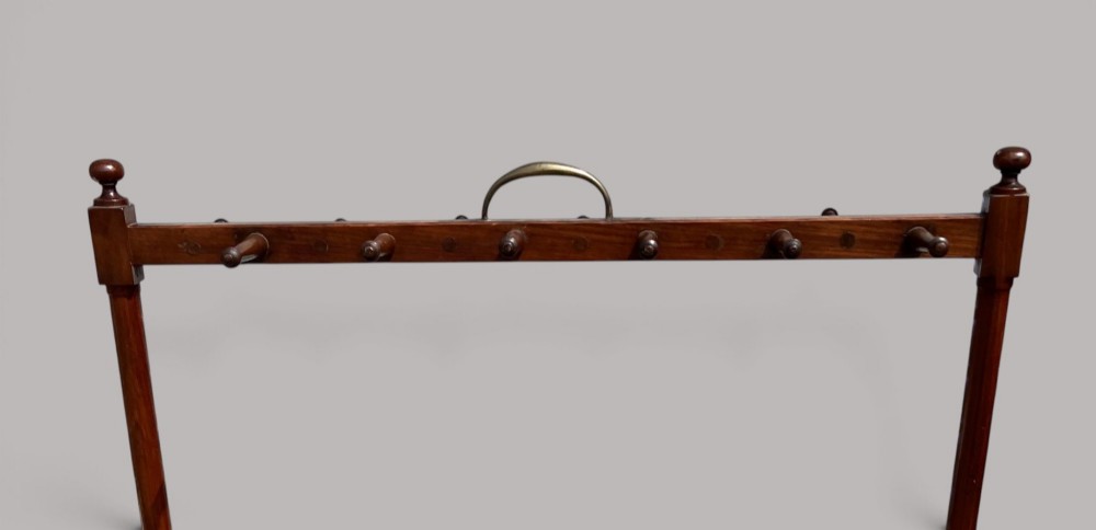 An antique mahogany whip and boot stand featuring turned upper pegs, a brass handle, shaped middle boot apertures, and swept trestle feet. View VII