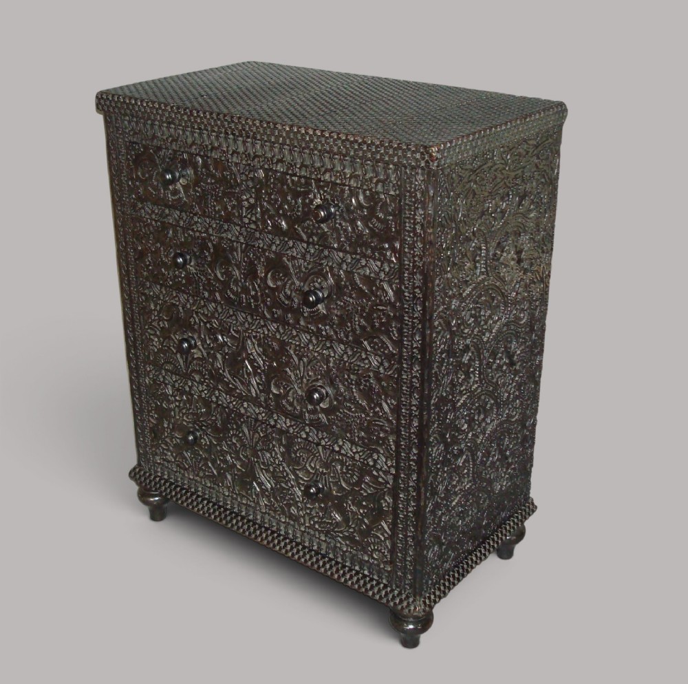 A 19th-century small ebonised chest of drawers featuring relief foliage carving across all surfaces, turned wooden knobs, and short bun feet.