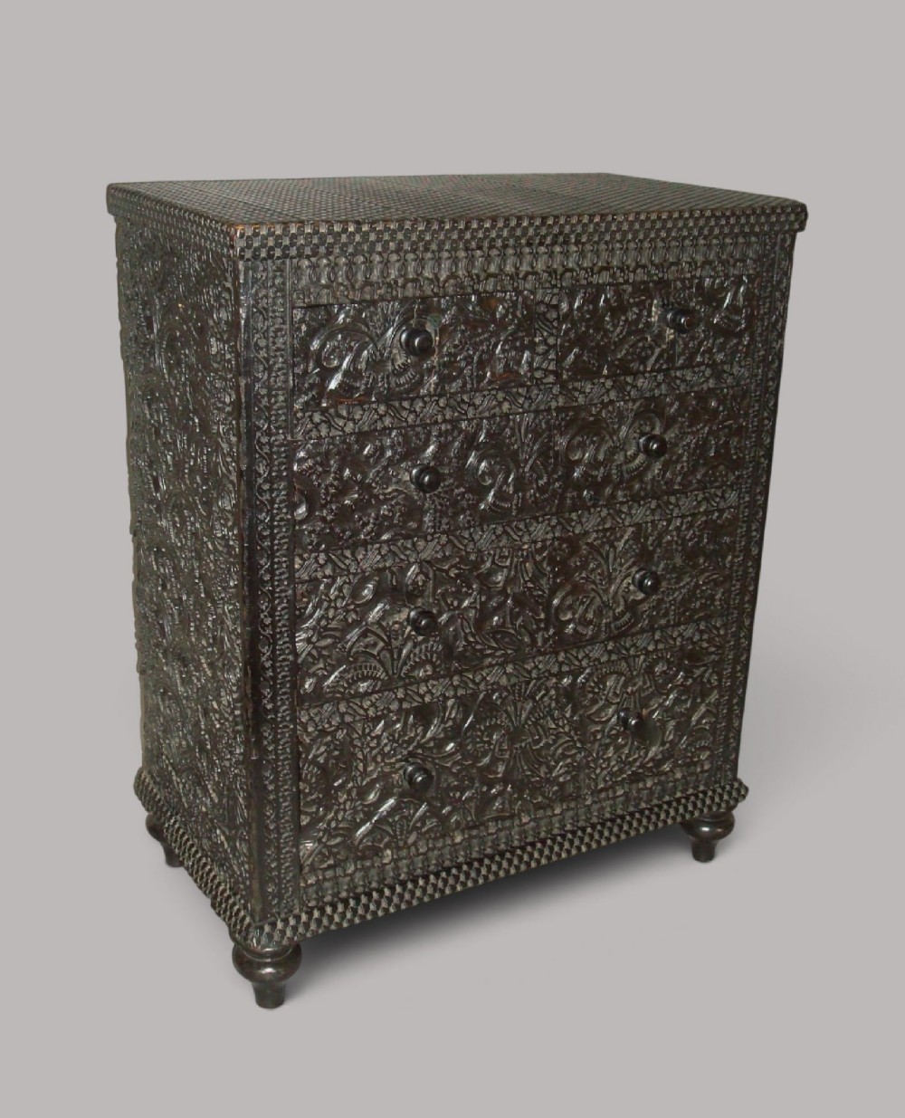 A 19th-century small ebonised chest of drawers featuring relief foliage carving across all surfaces, turned wooden knobs, and short bun feet. View II