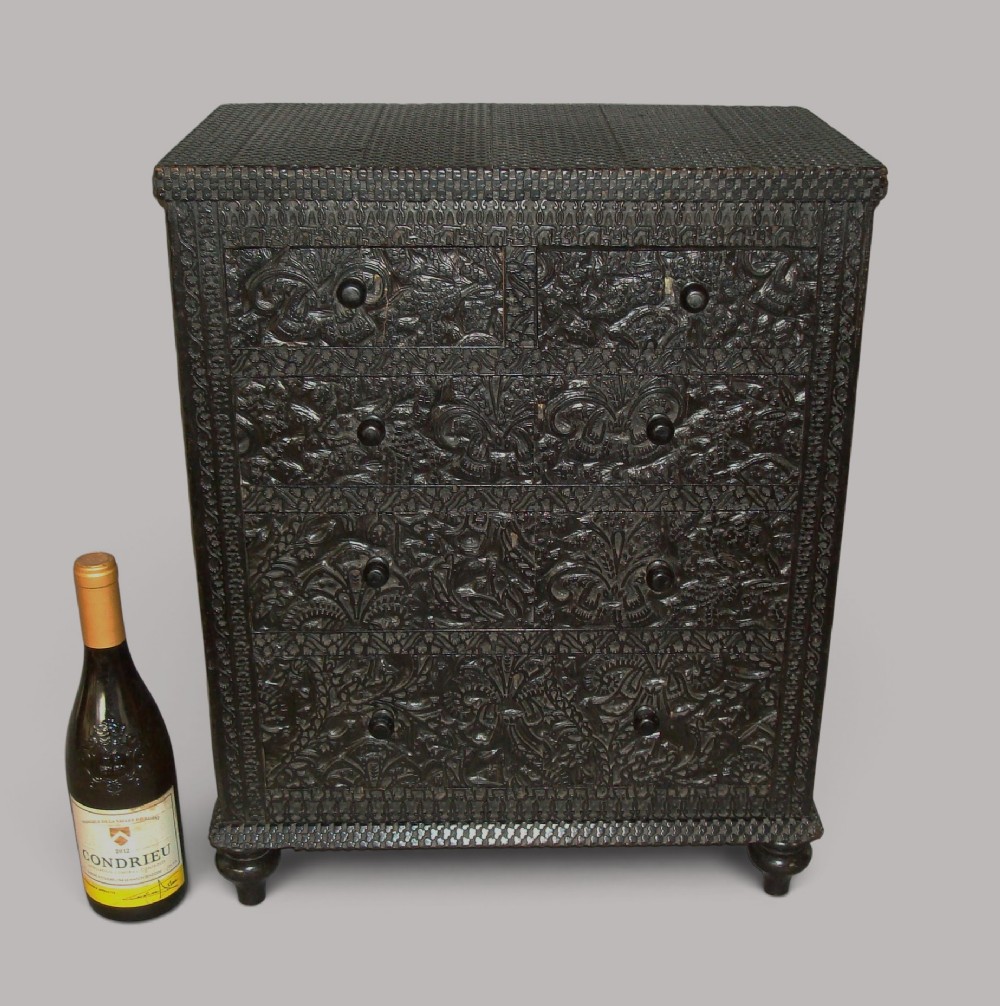 A 19th-century small ebonised chest of drawers featuring relief foliage carving across all surfaces, turned wooden knobs, and short bun feet. View III