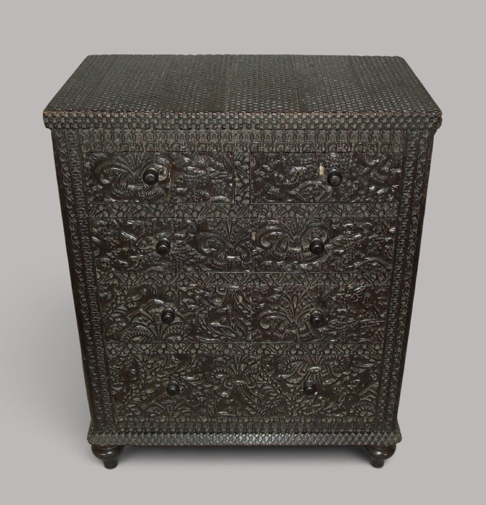 A 19th-century small ebonised chest of drawers featuring relief foliage carving across all surfaces, turned wooden knobs, and short bun feet. View IV
