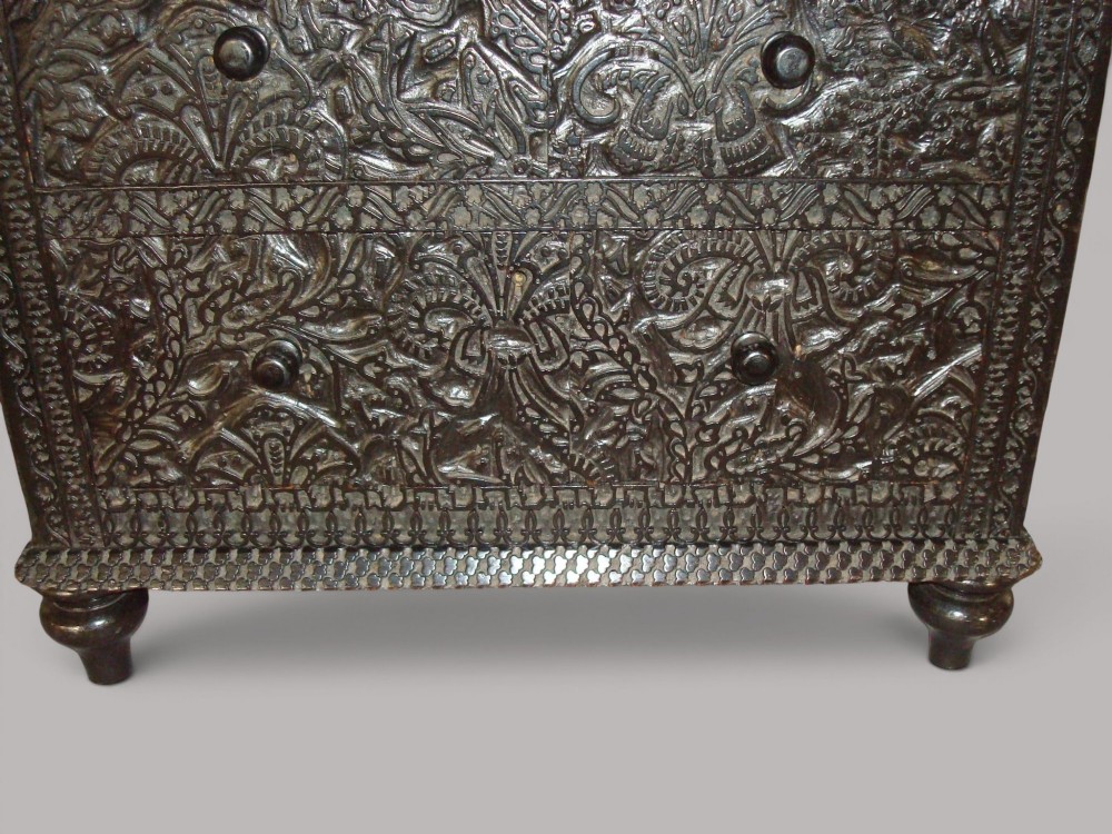 A 19th-century small ebonised chest of drawers featuring relief foliage carving across all surfaces, turned wooden knobs, and short bun feet. View V