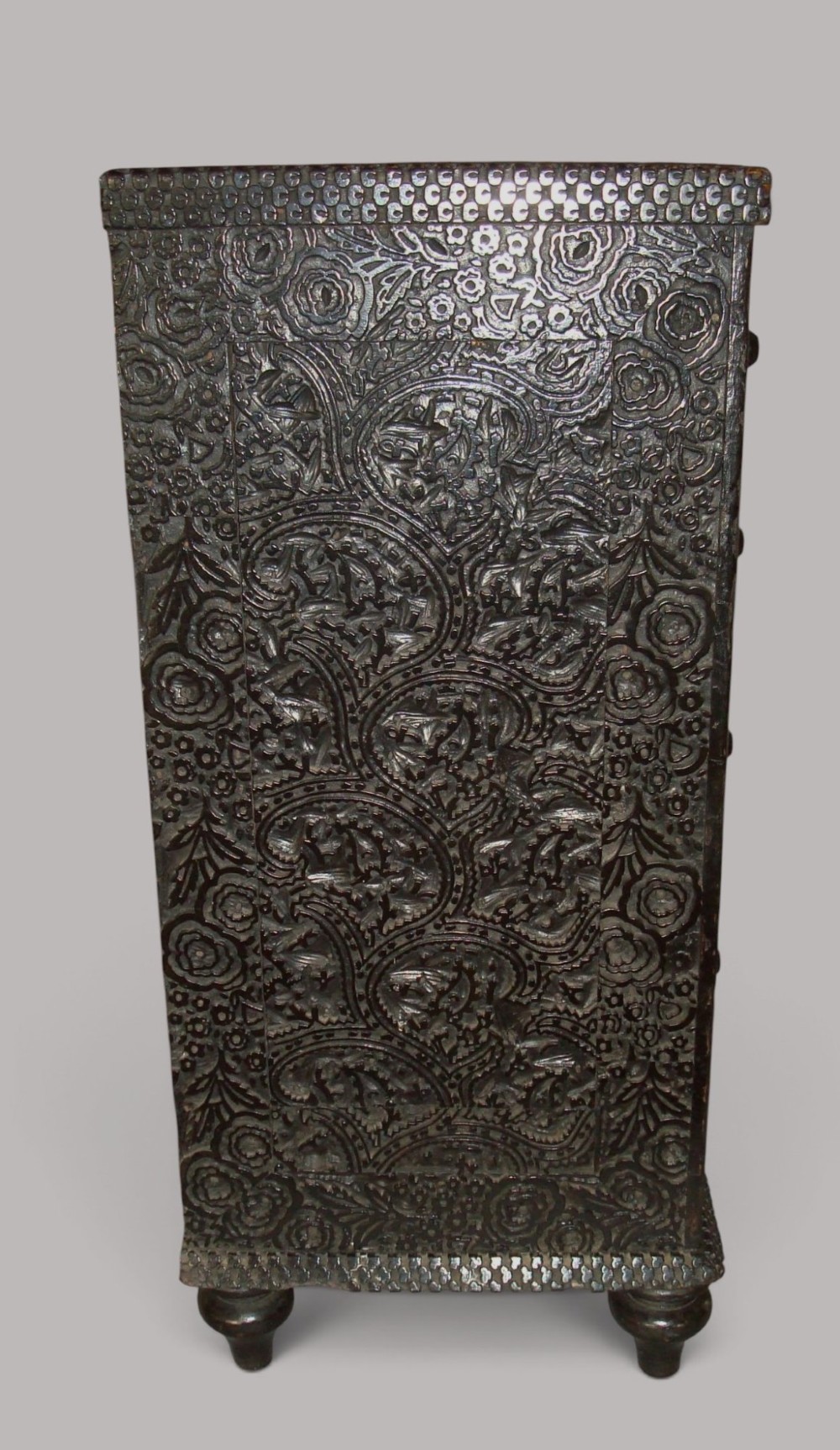 A 19th-century small ebonised chest of drawers featuring relief foliage carving across all surfaces, turned wooden knobs, and short bun feet. View VI