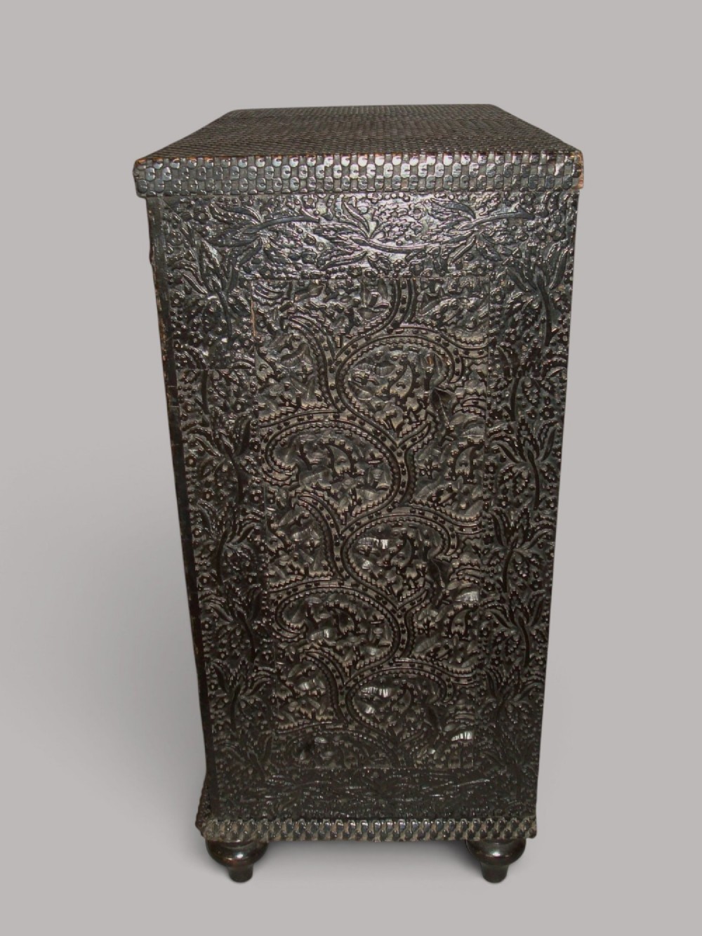 A 19th-century small ebonised chest of drawers featuring relief foliage carving across all surfaces, turned wooden knobs, and short bun feet. View VII
