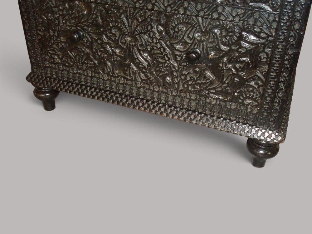 A 19th-century small ebonised chest of drawers featuring relief foliage carving across all surfaces, turned wooden knobs, and short bun feet. View IX