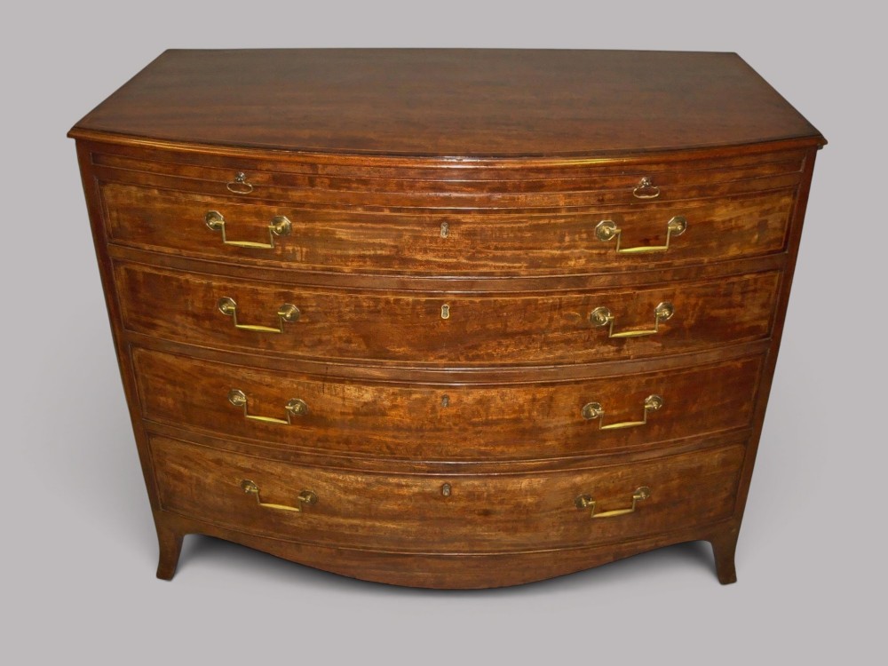 A George III mahogany bowfront chest of drawers featuring four graduated drawers with brass handles and splay feet. View IV
