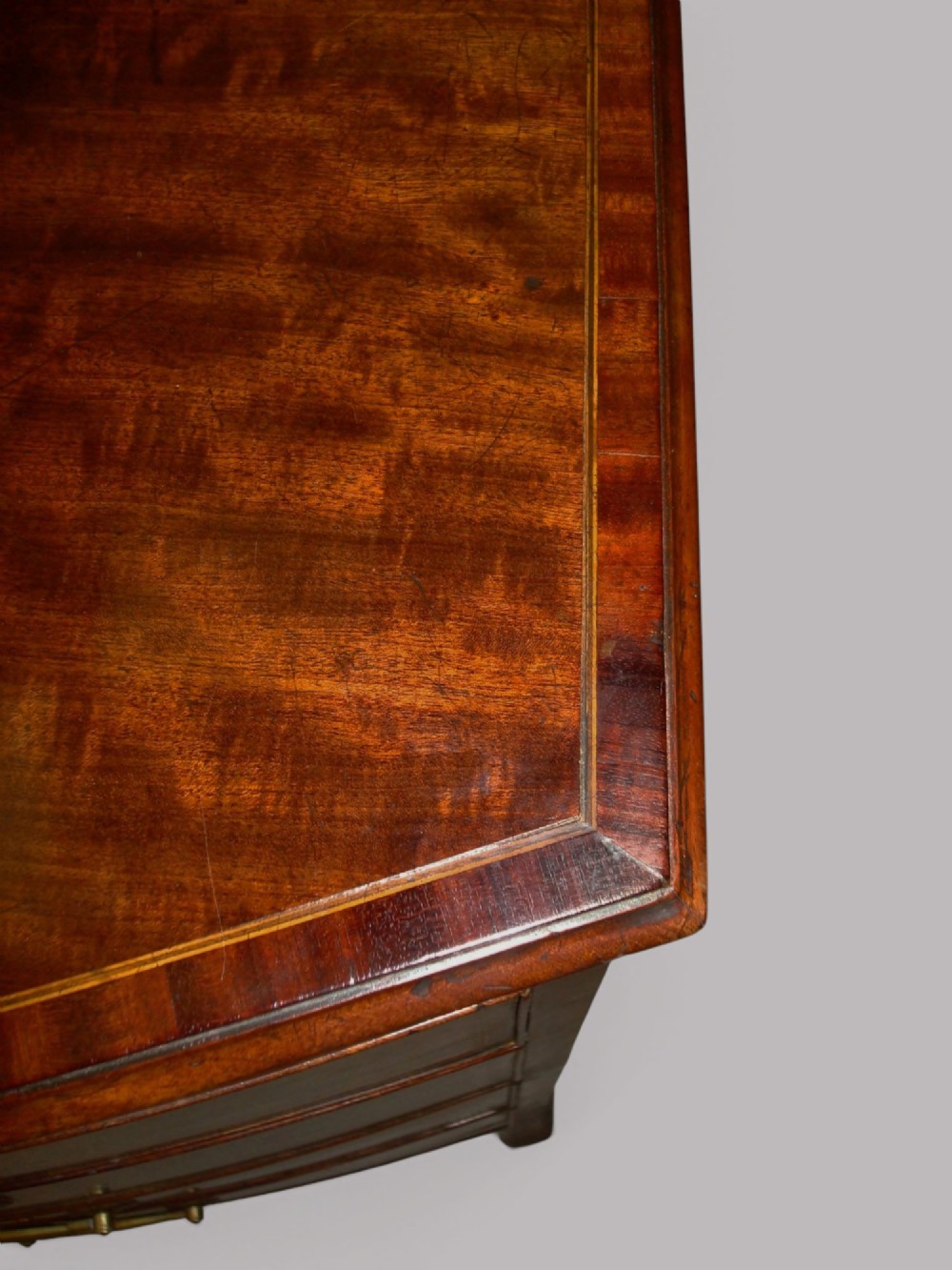 A George III mahogany bowfront chest of drawers featuring four graduated drawers with brass handles and splay feet. View VI