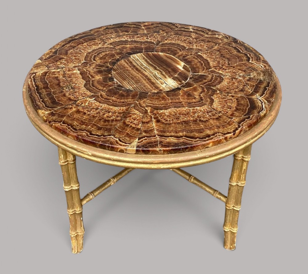 A circular late 19th-century low table featuring a variegated brown onyx stone top set within a giltwood frame with carved faux-bamboo legs.
