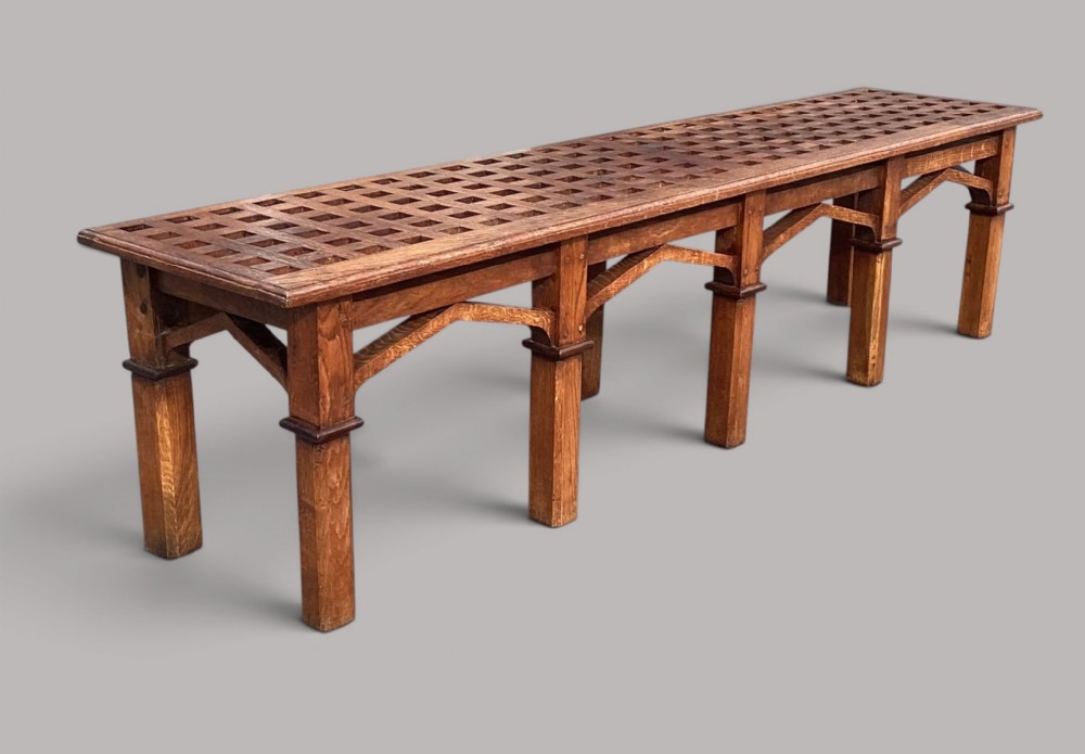 A long nineteenth-century oak hall bench featuring a lattice-work top supported by six square legs with arched spandrels.