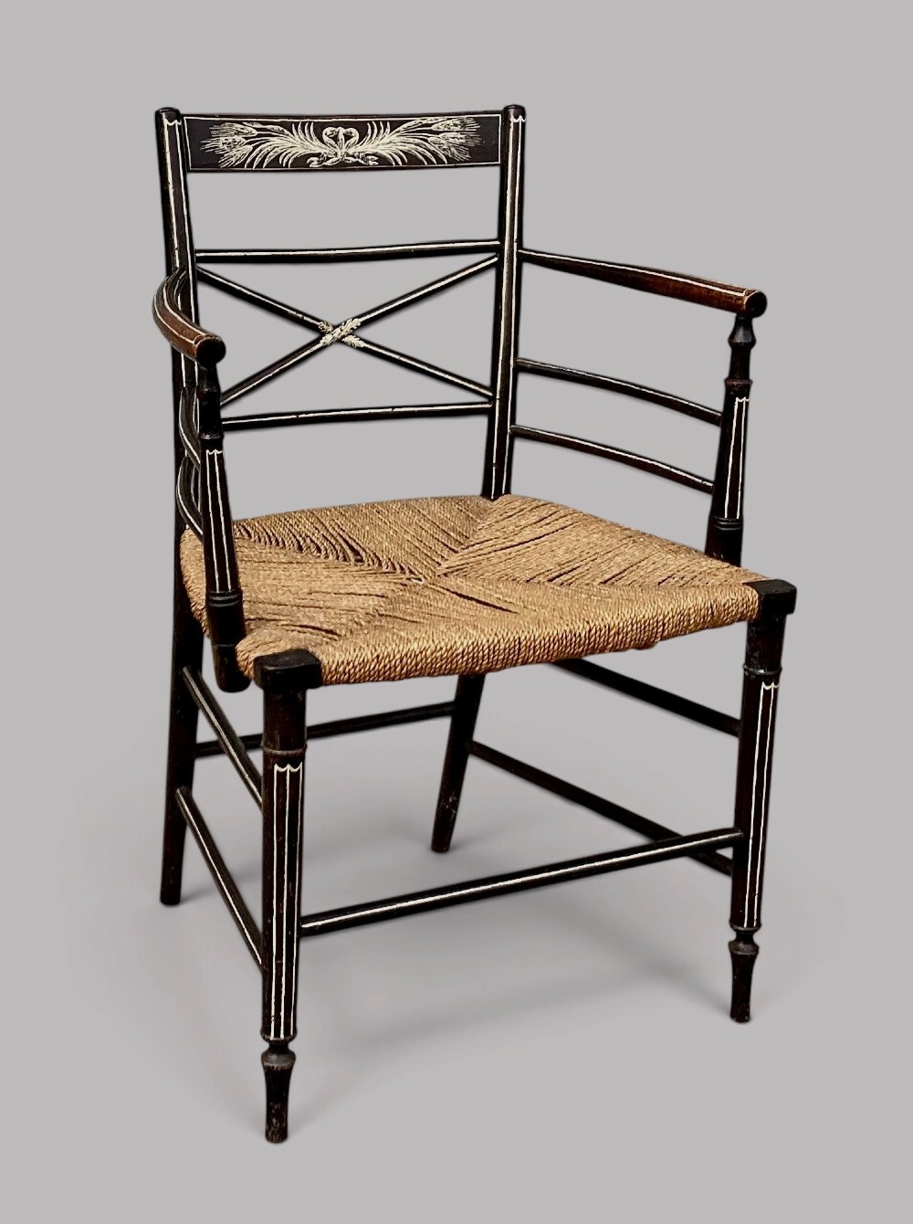 A Regency dark-painted wooden elbow chair featuring hand-painted white line decoration, an X-back splat, and a woven rush seat.