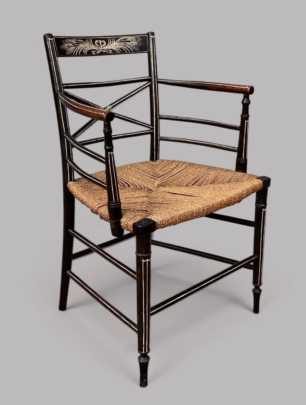 A Regency dark-painted wooden elbow chair featuring hand-painted white line decoration, an X-back splat, and a woven rush seat. View V