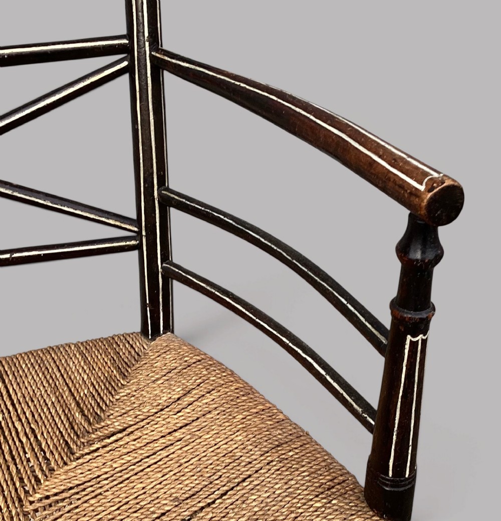 A Regency dark-painted wooden elbow chair featuring hand-painted white line decoration, an X-back splat, and a woven rush seat. View X