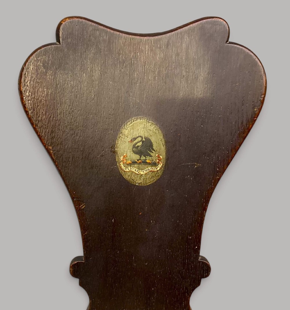 A pair of dark brown 18th-century Irish oak sgabello hall chairs with shaped backs featuring painted armorial crests. View II