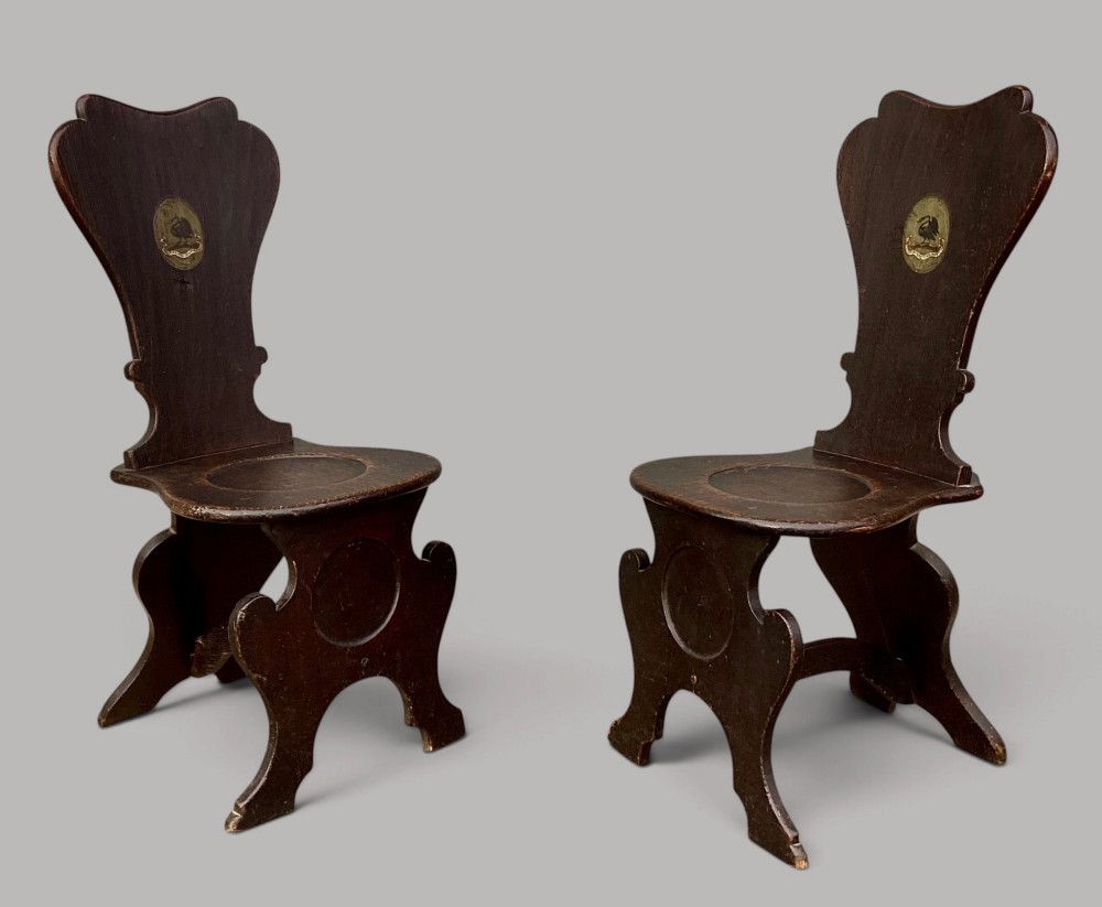 A pair of dark brown 18th-century Irish oak sgabello hall chairs with shaped backs featuring painted armorial crests. View III