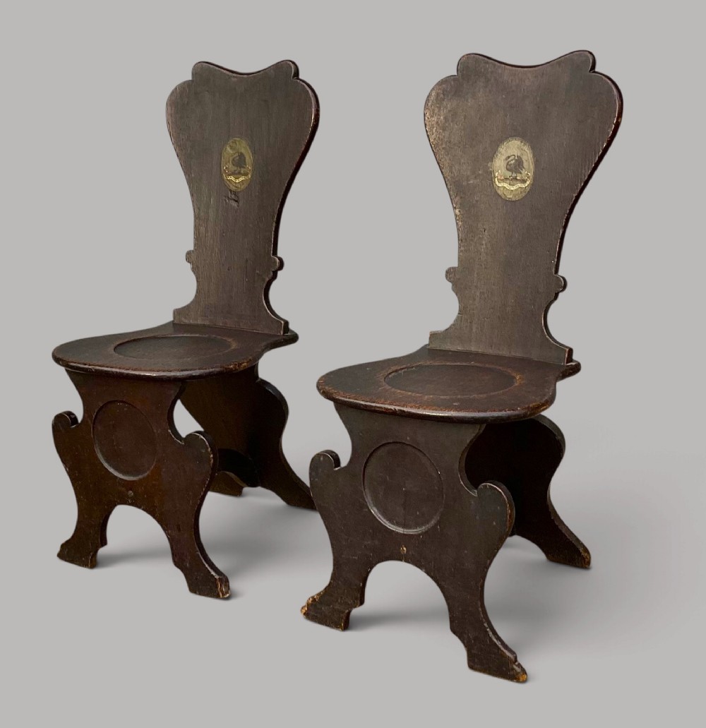 A pair of dark brown 18th-century Irish oak sgabello hall chairs with shaped backs featuring painted armorial crests. View IV