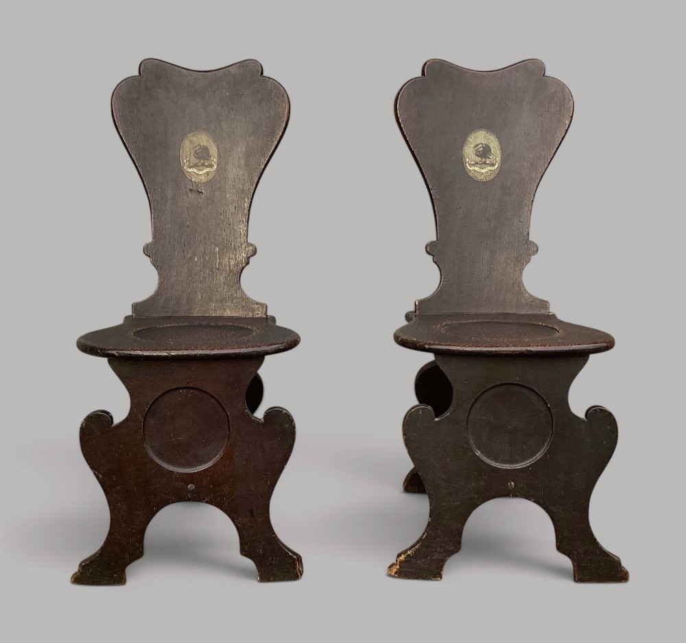 A pair of dark brown 18th-century Irish oak sgabello hall chairs with shaped backs featuring painted armorial crests. View V