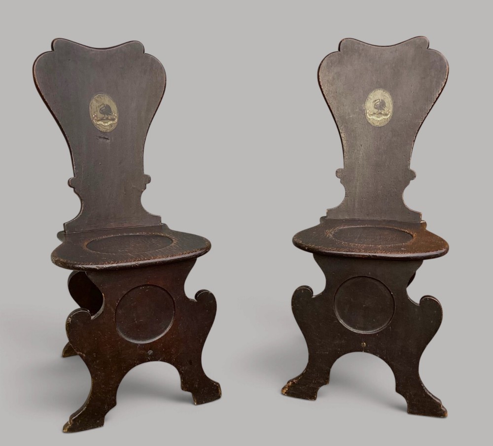 A pair of dark brown 18th-century Irish oak sgabello hall chairs with shaped backs featuring painted armorial crests. View VII