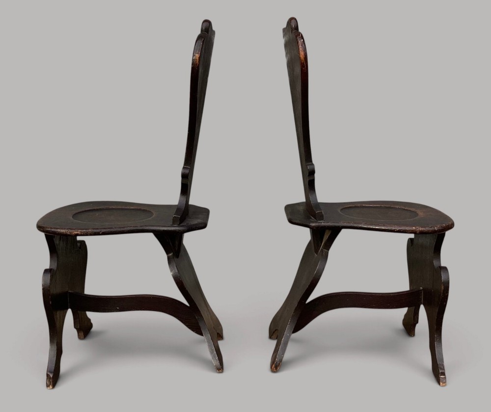 A pair of dark brown 18th-century Irish oak sgabello hall chairs with shaped backs featuring painted armorial crests. View VIII