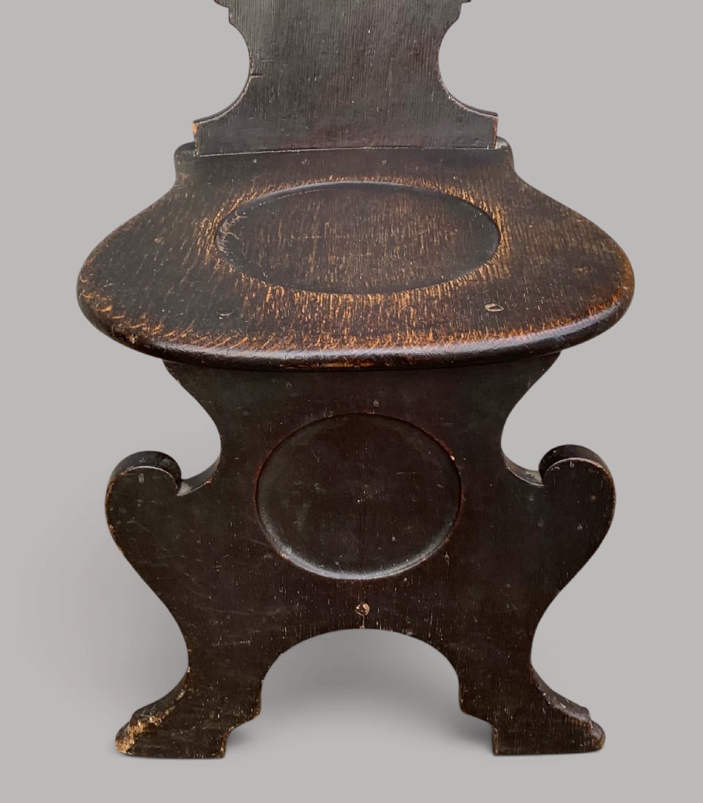 A pair of dark brown 18th-century Irish oak sgabello hall chairs with shaped backs featuring painted armorial crests. View X