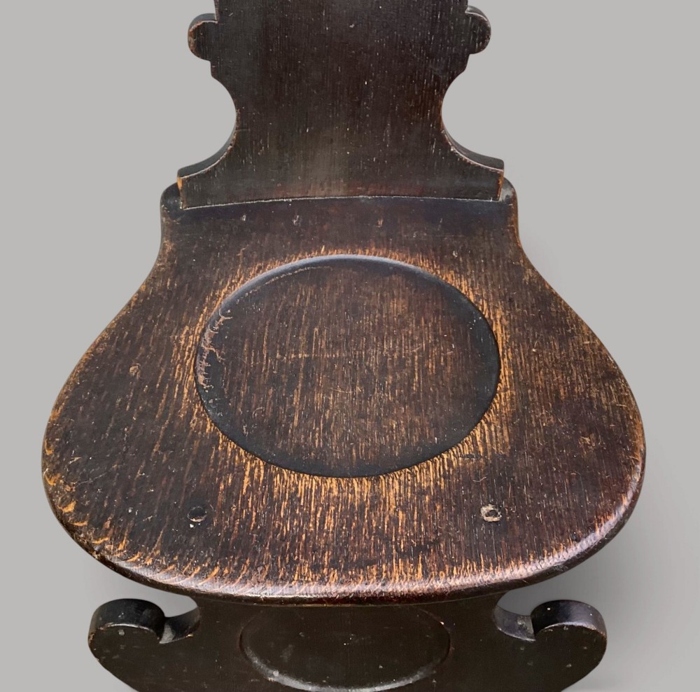 A pair of dark brown 18th-century Irish oak sgabello hall chairs with shaped backs featuring painted armorial crests. View XI