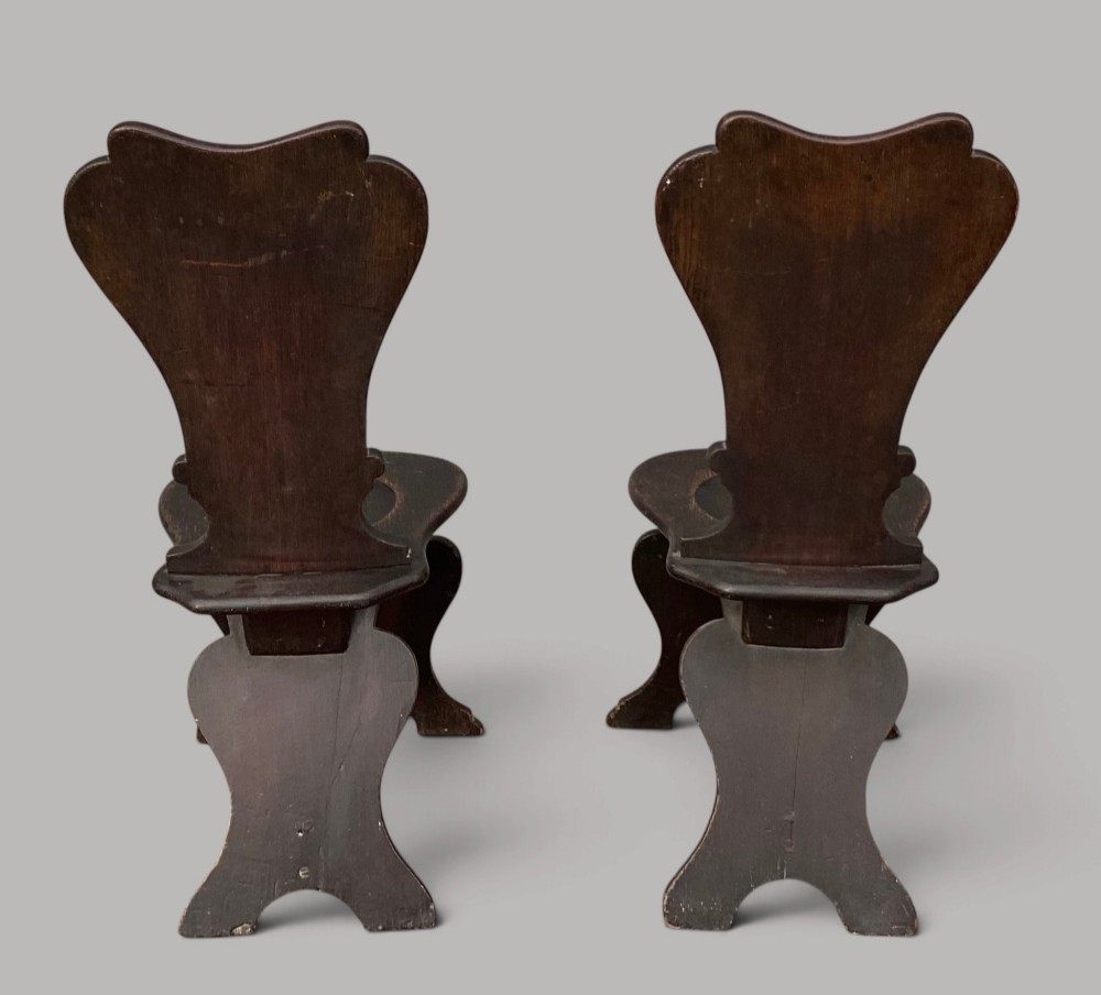 A pair of dark brown 18th-century Irish oak sgabello hall chairs with shaped backs featuring painted armorial crests. View XII