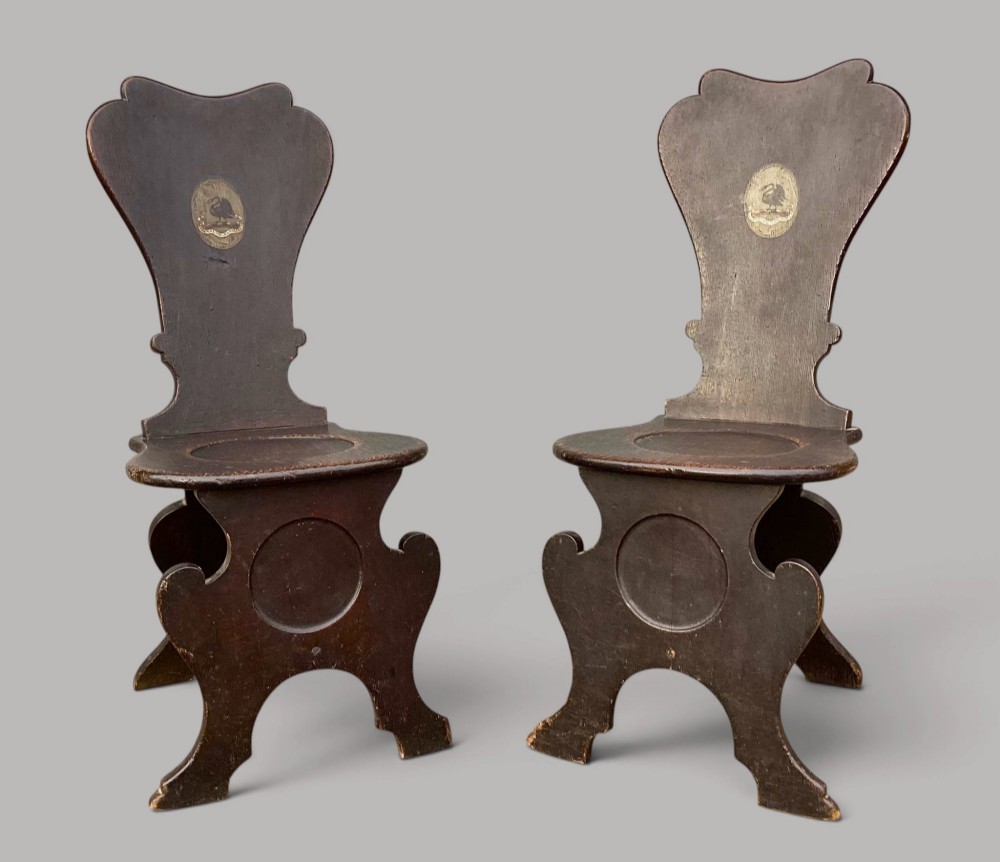 A pair of dark brown 18th-century Irish oak sgabello hall chairs with shaped backs featuring painted armorial crests. View XIII