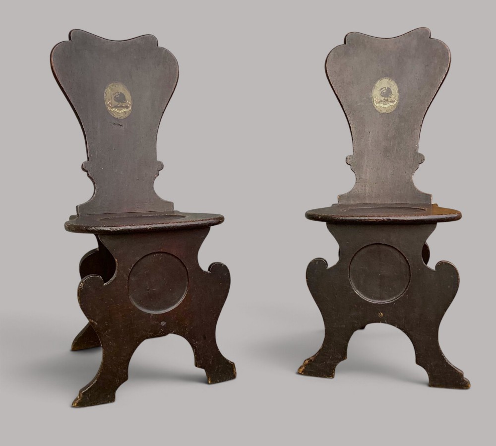 A pair of dark brown 18th-century Irish oak sgabello hall chairs with shaped backs featuring painted armorial crests. View XIV
