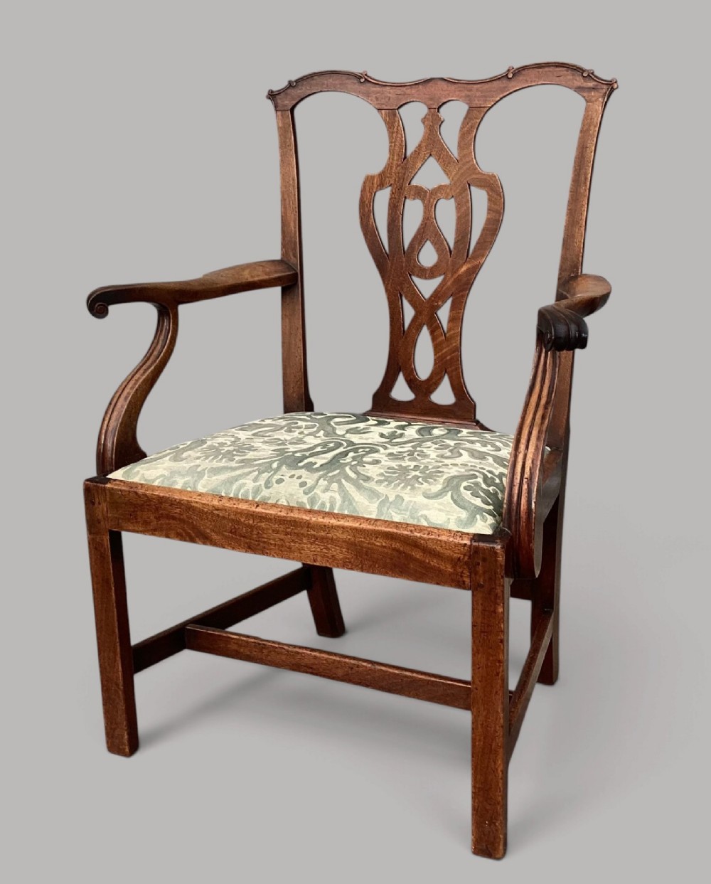 A George III mahogany open armchair featuring a carved pierced back splat, curved armrests, and a patterned fabric seat.
