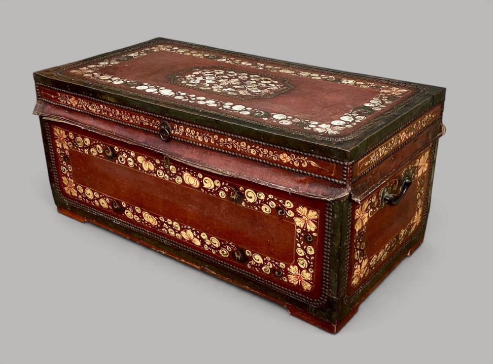 A 19th-century Chinese export camphor trunk bound in red leather with brass studding, gilded floral borders, and side carrying handles.