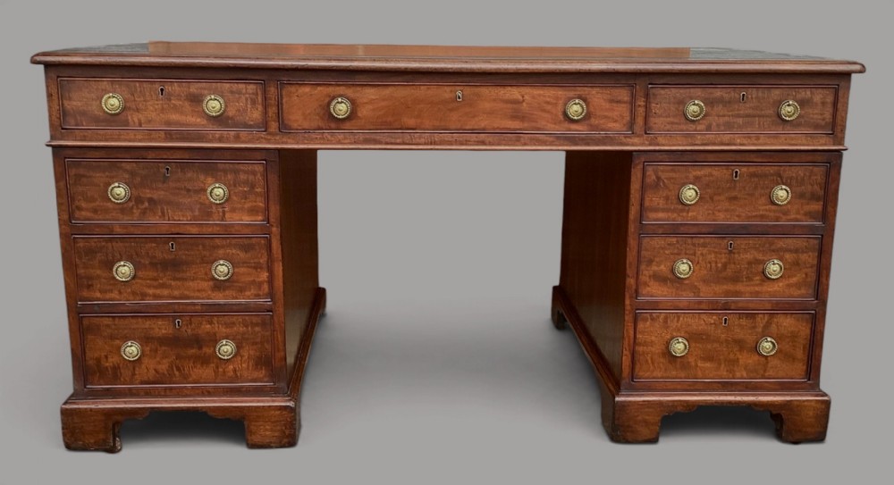 A Regency period mahogany pedestal desk featuring an inset writing surface, nine drawers with round brass handles, and plinth bases.