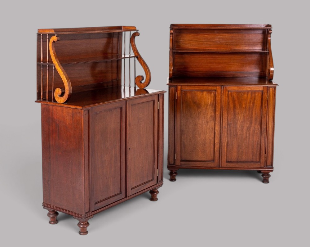 A matching pair of Regency mahogany side cabinets featuring panelled cupboard doors and tiered upper shelves supported by carved scroll uprights.