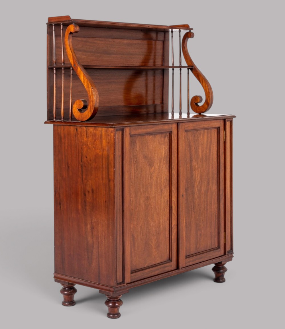A matching pair of Regency mahogany side cabinets featuring panelled cupboard doors and tiered upper shelves supported by carved scroll uprights. View II