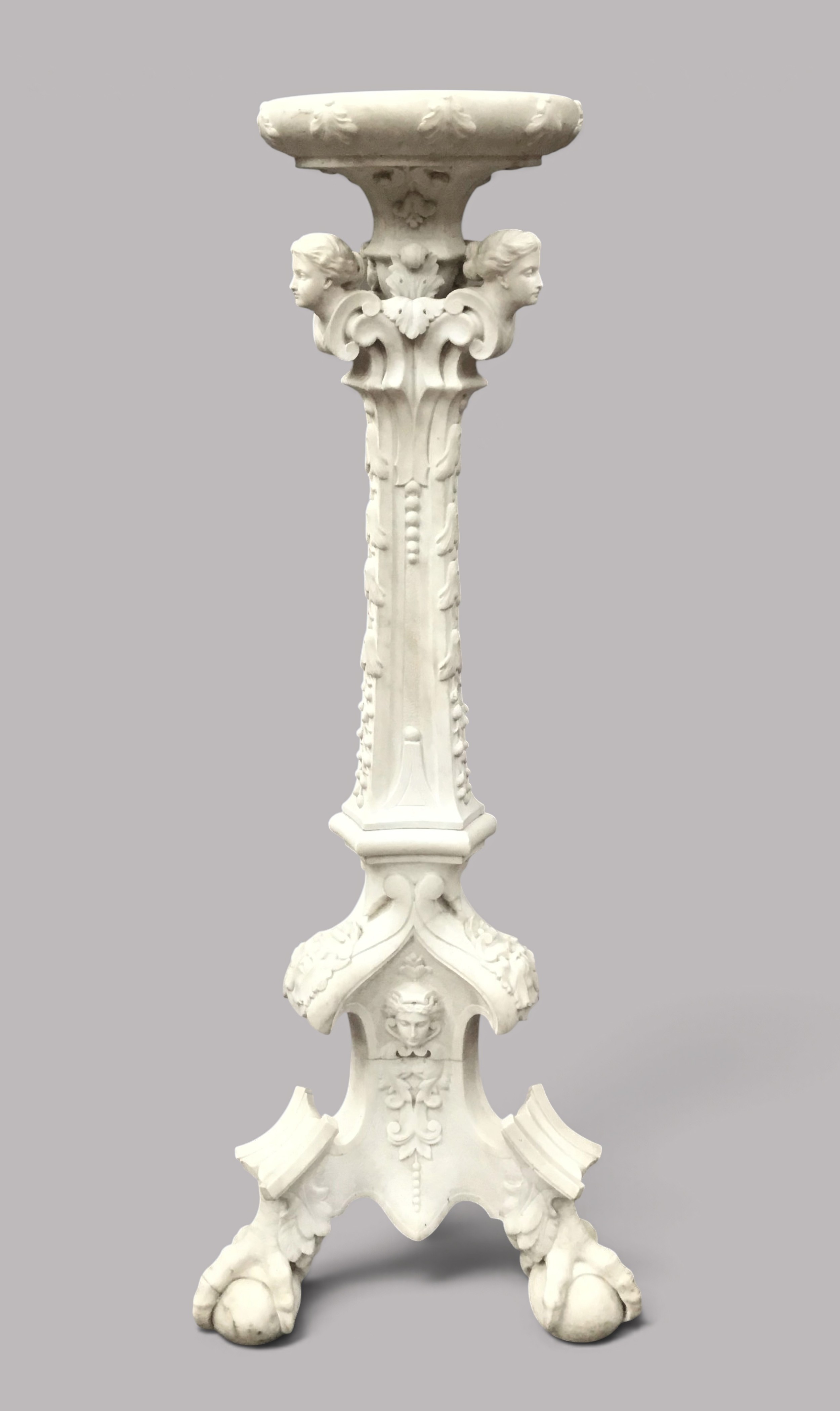 A nineteenth-century carved white Carrara marble torchere stand featuring classical maiden heads, elaborate foliate carvings, a fluted column, and claw feet.