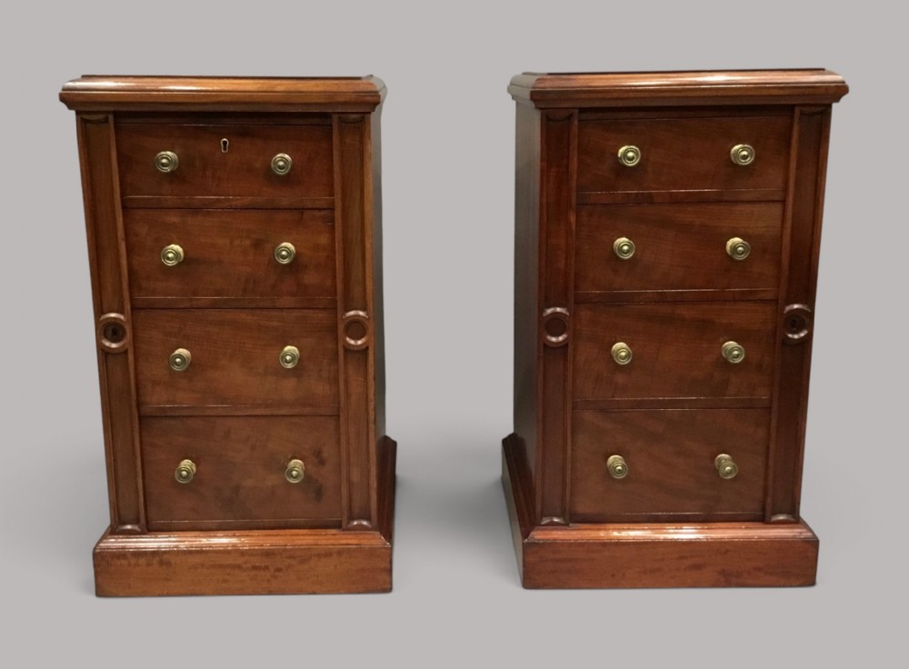 A pair of tall, narrow mahogany Wellington chests featuring four drawers each, turned brass knobs, and carved roundel pilasters on plinth bases.