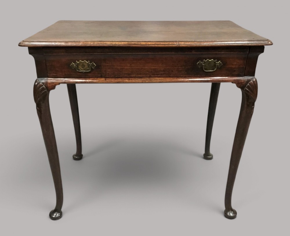 A George II dark walnut side table featuring carved shell knees on slender cabriole legs with pad feet and a single drawer with brass handles.
