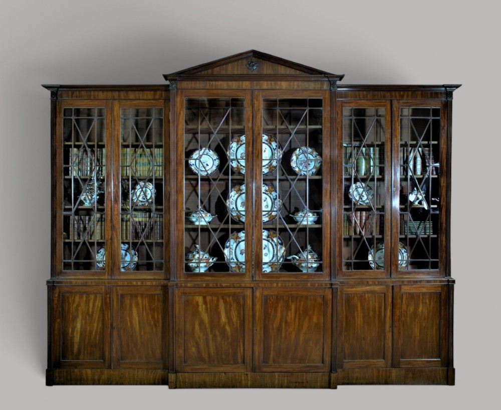 A large George III mahogany breakfront bookcase with a central pediment, glazed upper doors with geometric glazing bars, and flame mahogany cupboard doors below.