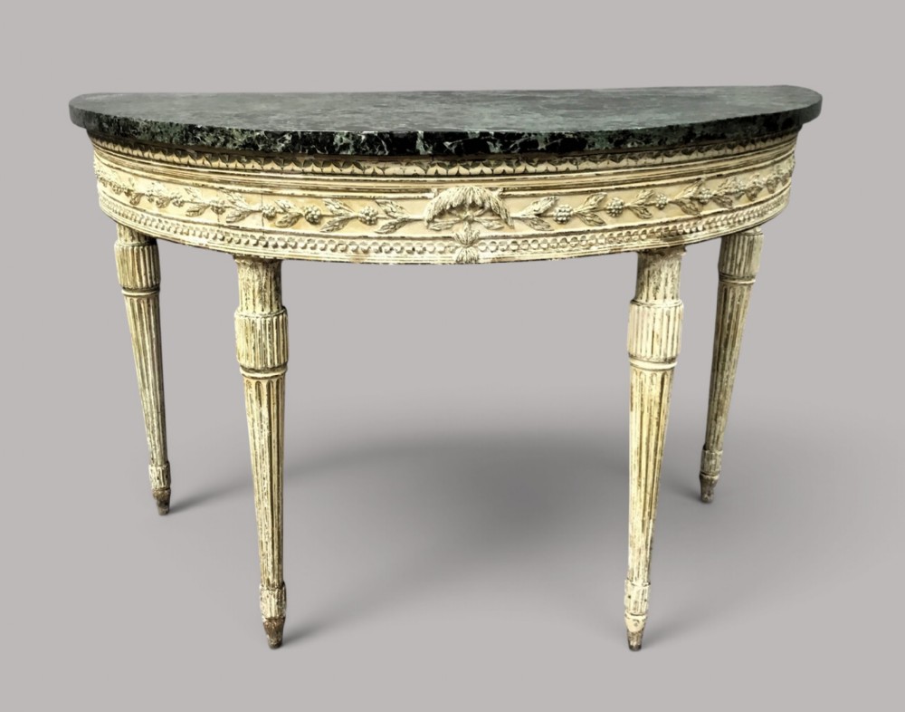 An 18th-century Italian Neoclassical demilune console table featuring an off-white painted timber frame with fluted tapered legs and a dark green marble top.