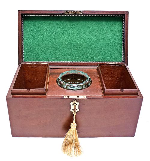 fig 2. An open rectangular dark wood tea caddy featuring two internal covered compartments, a central cut glass mixing bowl, a green fabric-lined lid, and a key with a tassel inserted in the front lock.