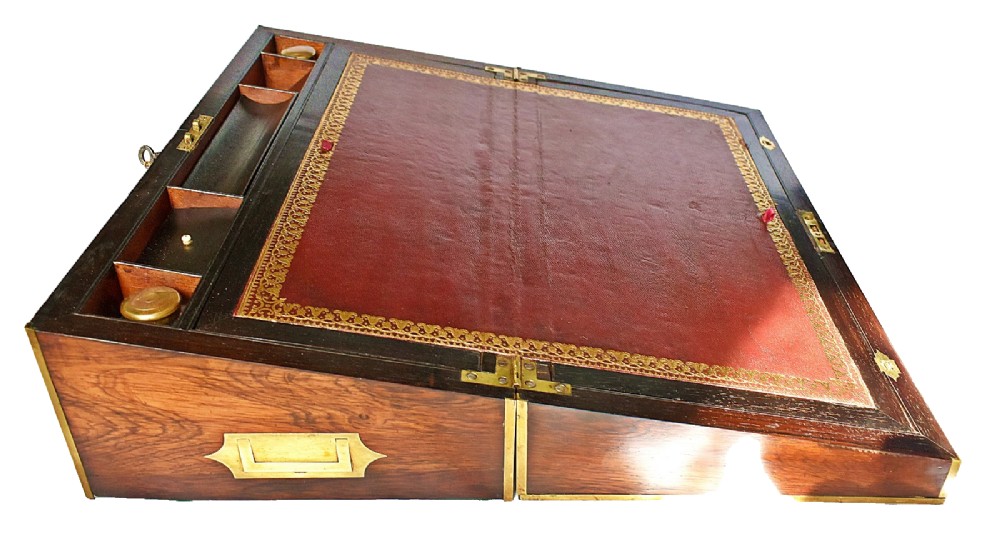 An open antique mahogany writing slope featuring a red gold-tooled leather writing surface, brass corner mounts, and dedicated compartments for inkwells. View VI