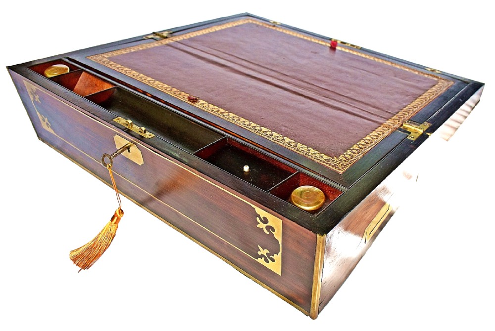 An open antique mahogany writing slope featuring a red gold-tooled leather writing surface, brass corner mounts, and dedicated compartments for inkwells. View VII