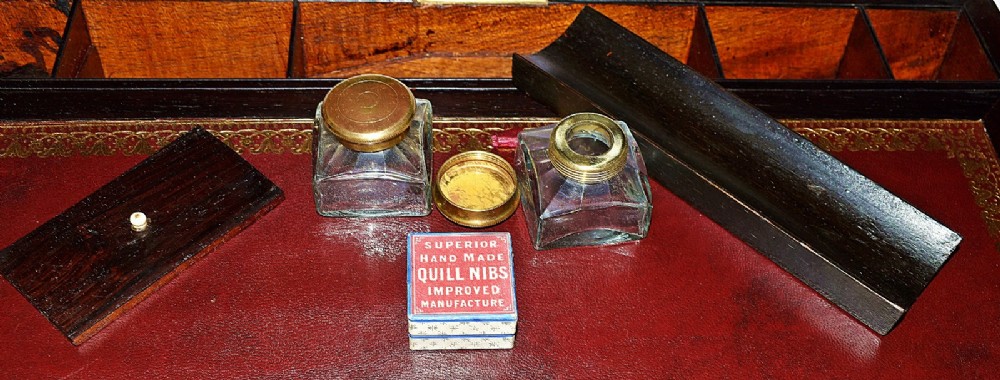 An open antique mahogany writing slope featuring a red gold-tooled leather writing surface, brass corner mounts, and dedicated compartments for inkwells. View XI