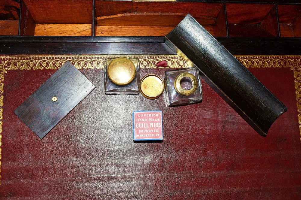 An open antique mahogany writing slope featuring a red gold-tooled leather writing surface, brass corner mounts, and dedicated compartments for inkwells. View XII